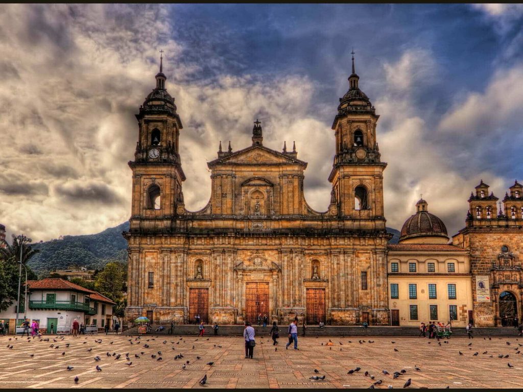 This is the main Cathedral in Bogota, Colombia, called Catedral Primada. It is in the East side of the Plaza de Bolivar.
ISO 100, 15mm, f9, (1/800, 1/200, 1/50) handheld. HDR processing in Photomatix using Details Enhancer and Light mode. Imagenomics Noiseware, in PS Smart Sharpen, and Freaky Details. The warm colors came from Nik Color Efex  Skylight and Indian Summer filters. I colored the sky blue using Nik Viveza 2 as Photomatix had produced the typical darkish desaturated blue. It often does this, note that the shirts of the people walking in the plaza are actually white.