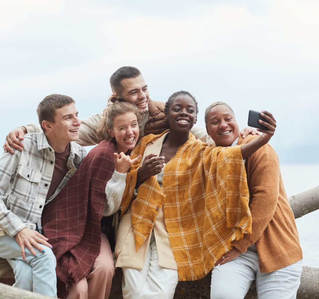 Minimal shot of diverse group of young people taking selfie on beach in Autumn, copy space